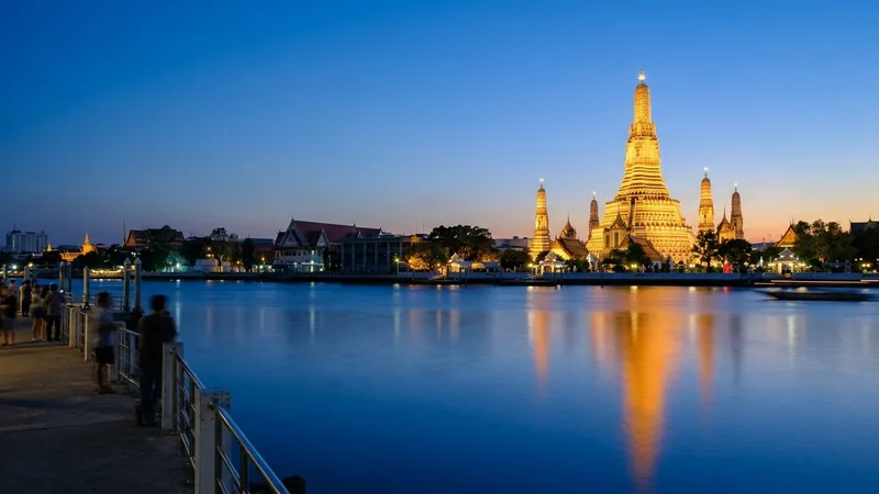 Illuminated Wat Arun temple reflected in the Chao Phraya River at blue hour.