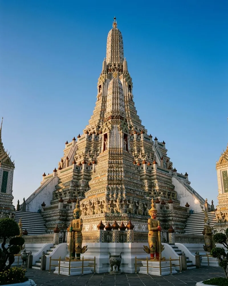 Vertical view of Wat Arun's ornate porcelain-covered central spire against blue sky.