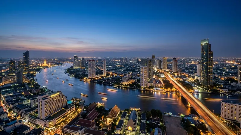 Bangkok skyline and curving Chao Phraya River at dusk from a high rooftop.
