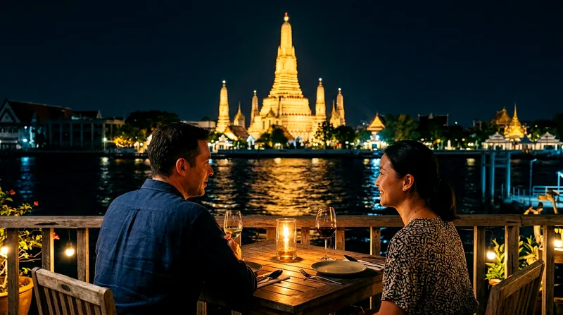 Couple at riverside restaurant table watching illuminated Wat Arun at night