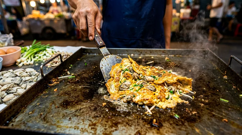 Vendor flipping oyster omelette on a flat griddle with spatula