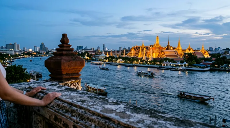 View from Wat Arun's upper balcony across Chao Phraya toward Grand Palace at dusk
